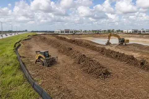 Pair of unbranded machines working a multi-acre commercial clearing with mulch windrows and a retention pond dig underway